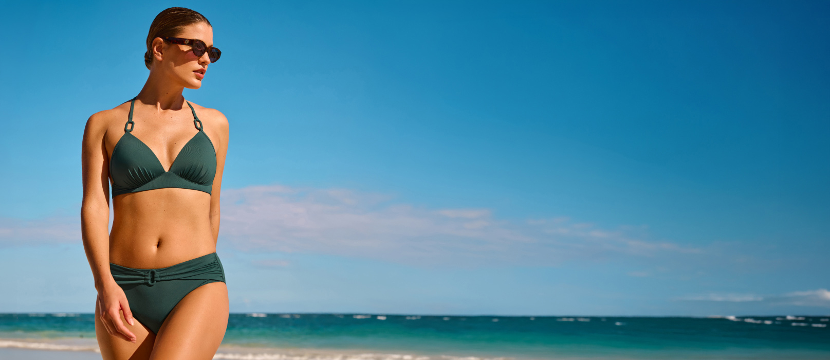 Woman walking on the beach and wearing a dark green bikini set from Costa Del Rey brand. 
